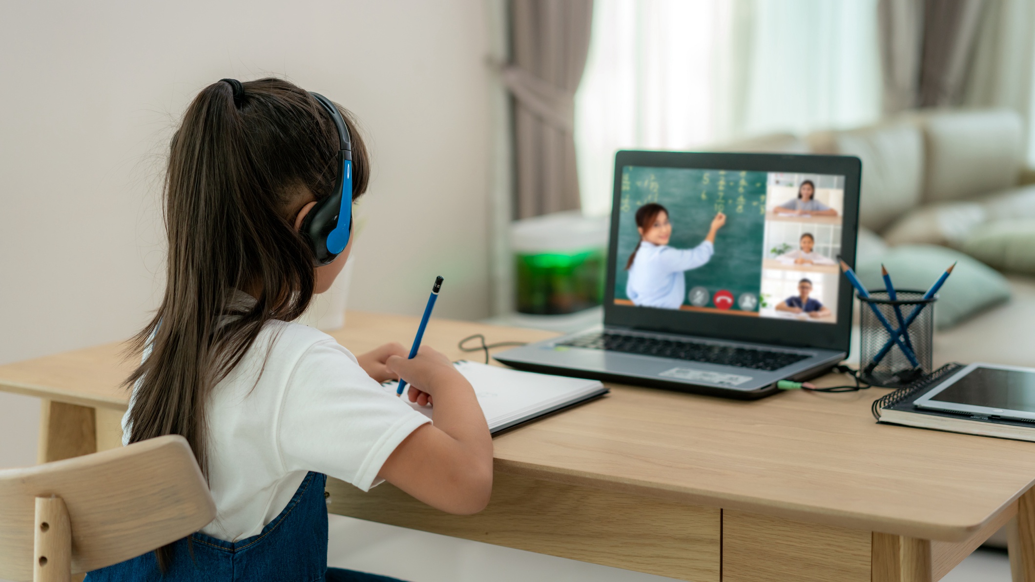 Asian girl student video conference e-learning with teacher and classmates on computer in living room at home. Homeschooling and distance learning ,online ,education and internet.